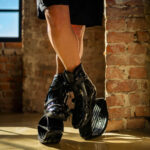 Close-up of a person standing with crossed legs while wearing Fit Boots Rebound Boots indoors.